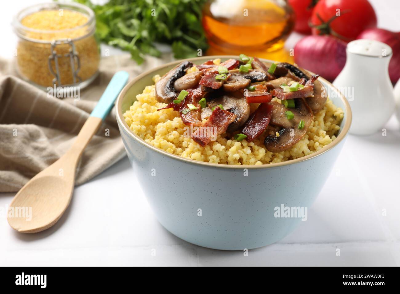 Savoureux porridge de millet avec des champignons, du bacon et de l'oignon vert dans un bol sur une table blanche, gros plan Banque D'Images