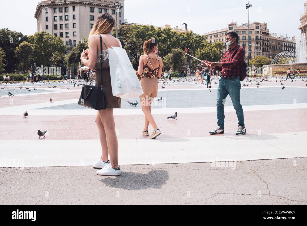 Barcelone, Espagne - 5 juin 2021 : un vendeur de rue tente de vendre un bâton à selfie à deux filles du shopping Banque D'Images
