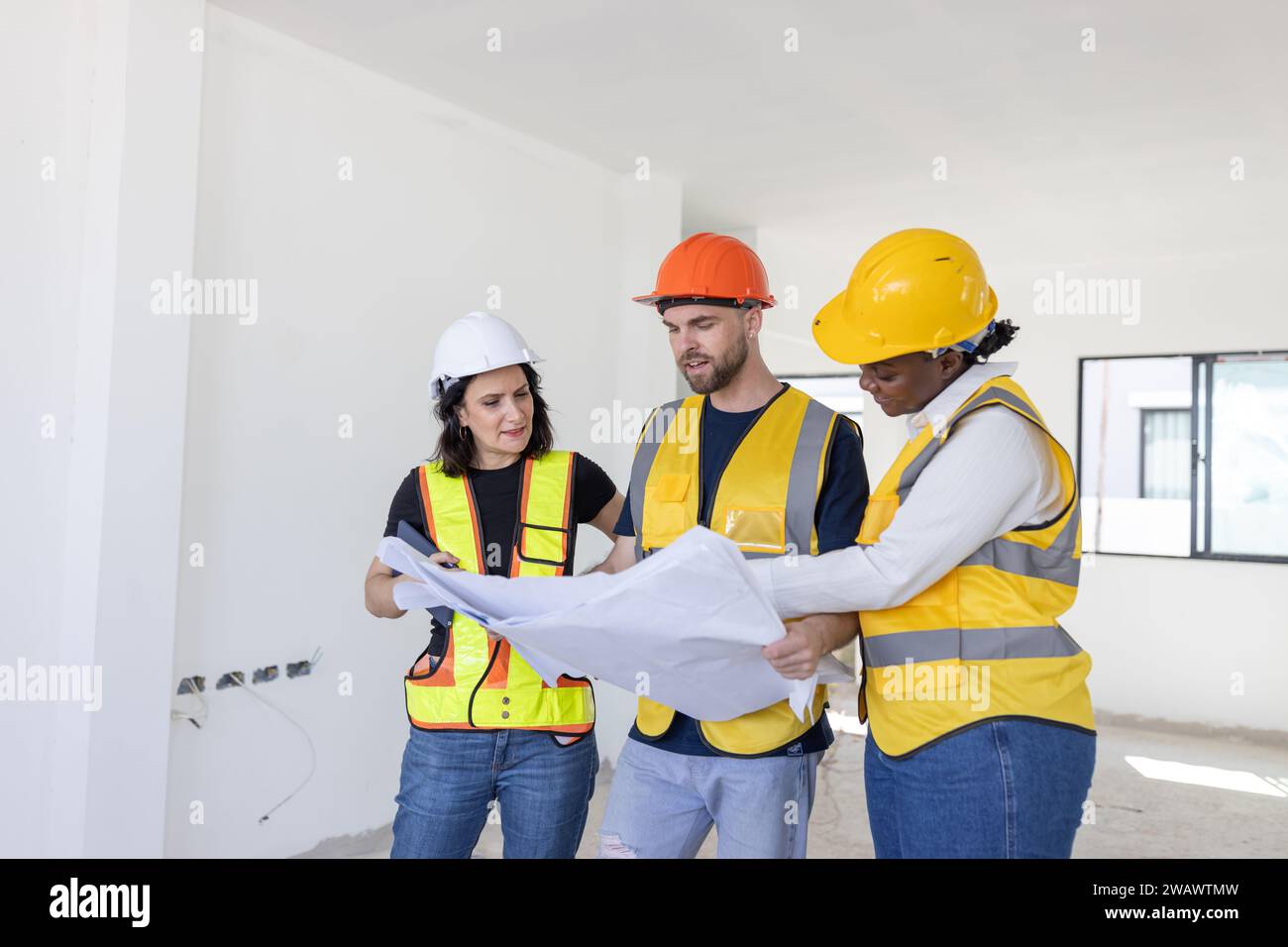 Groupe d'ingénieurs de travailleurs de la construction professionnels se réunissant debout ensemble travaillent dans le nouveau chantier de construction de maison avec le plan d'étage. Banque D'Images