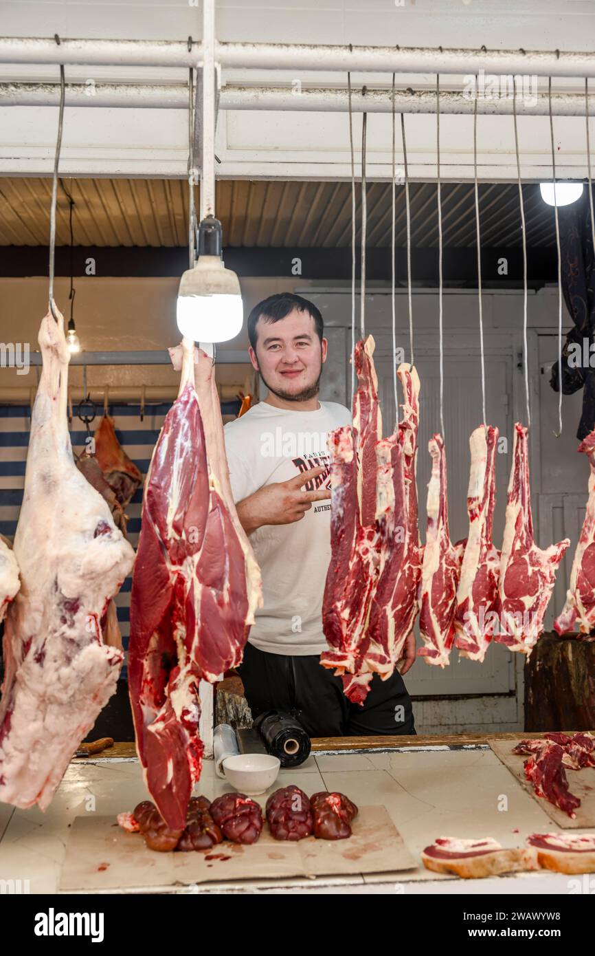 Boucher regardant à travers la viande suspendue, boucherie, au stand de marché pour les produits à base de viande, Uzgen Bazaar, Oesgoen, région d'Osh, Kirghizistan Banque D'Images