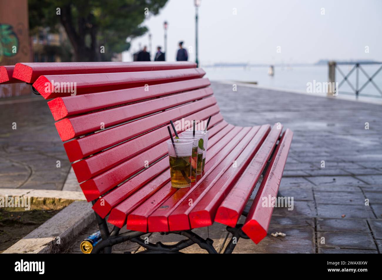 Des gobelets en plastique à moitié pleins de cocktails ont été laissés sur un banc rouge du parc après une nuit de fête. Banque D'Images