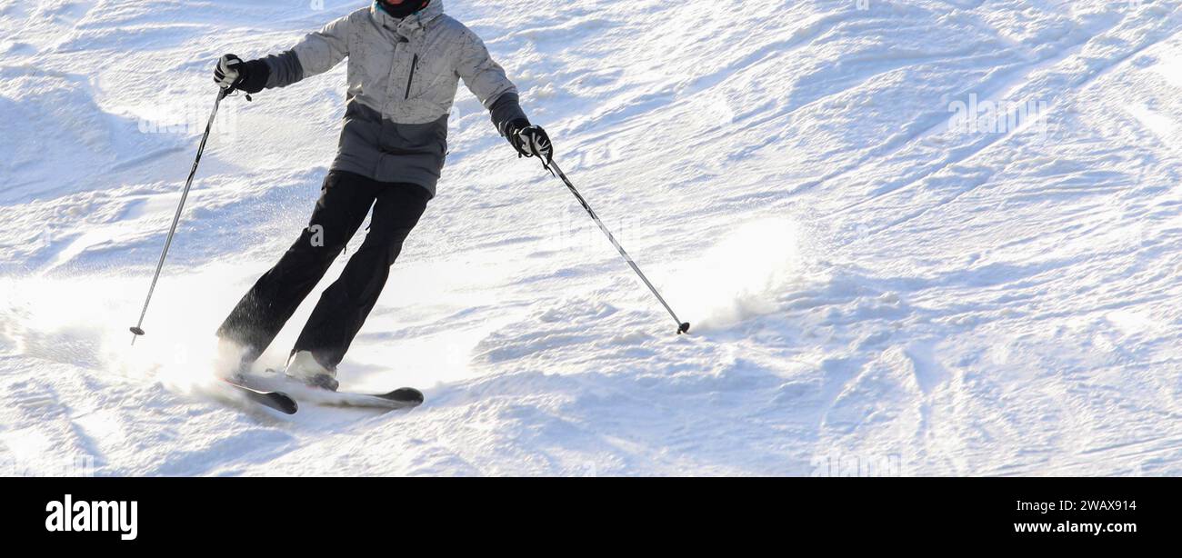 Un skieur individuel est capturé en mi-glisse alors qu'il navigue en descente douce sur une piste de ski enneigée bien foulée, baignée par un soleil éclatant sur le mont S. Banque D'Images