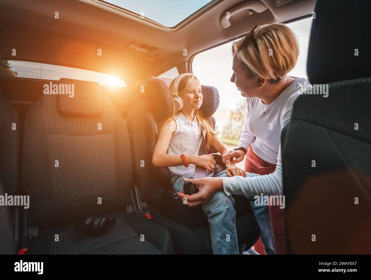 À l'intérieur de la photo de voiture d'une mère fixant avec la ceinture de sécurité automatique sa petite fille assise dans le siège d'enfant. Fille écoutant de la musique à l'aide d'écouteurs Banque D'Images