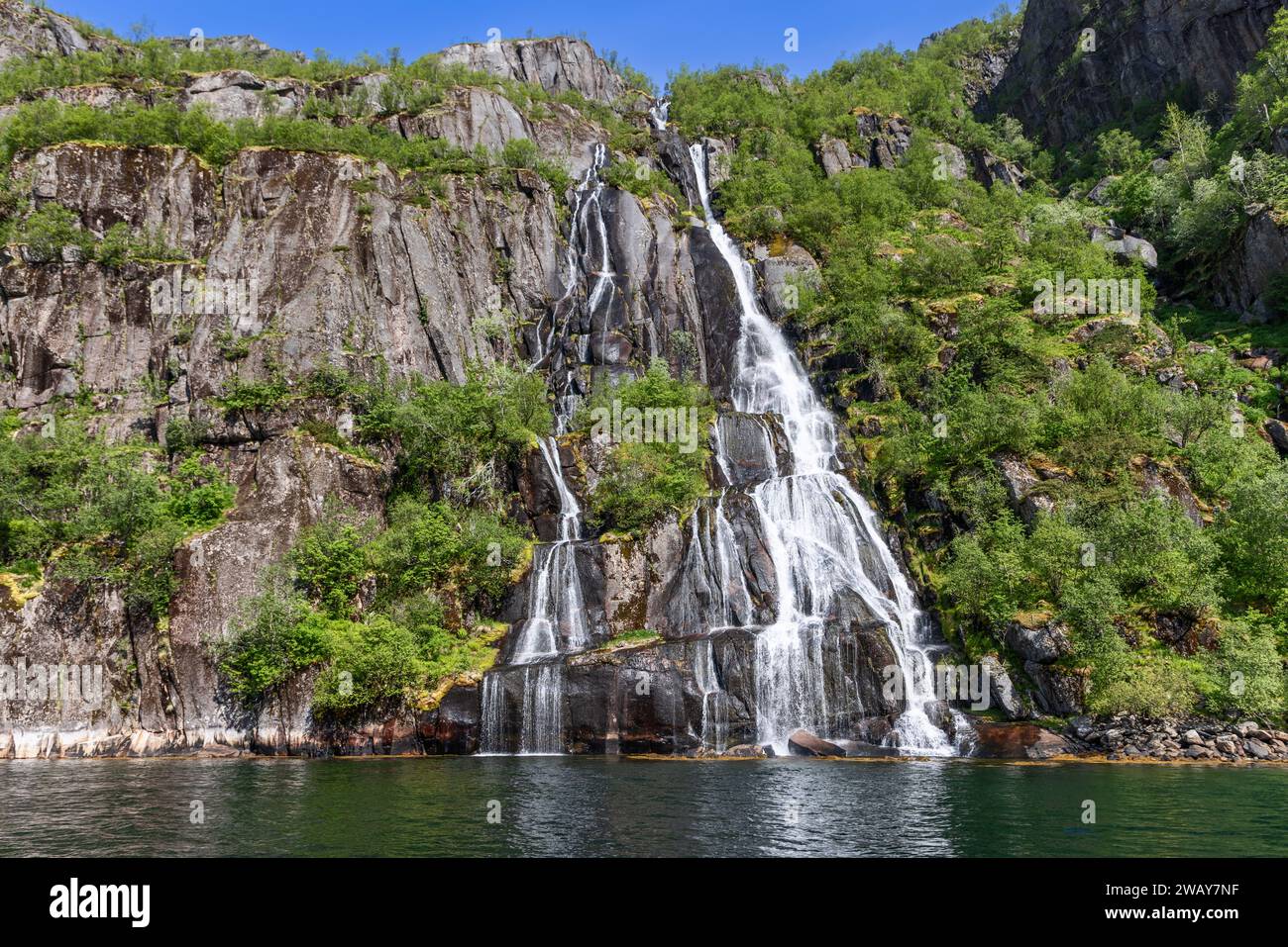 Sunlight danse sur les eaux en cascade d'une cascade à plusieurs niveaux dans le cadre verdoyant et luxuriant de Trollfjorden, Lofoten, Norvège Banque D'Images