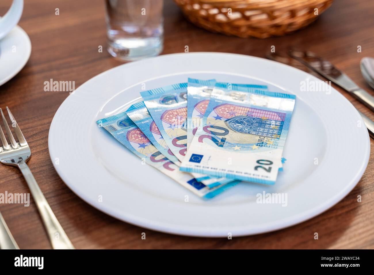 Bavière, Allemagne - 6 janvier 2024 : concept de coût de la nourriture et de gastronomie. Une table couchée avec une assiette blanche avec des billets en euros *** Kosten für Nahrung und Gastronomie Konzept. Ein gedeckter Tisch mit einem weißen Teller mit Euro Geldscheinen Banque D'Images