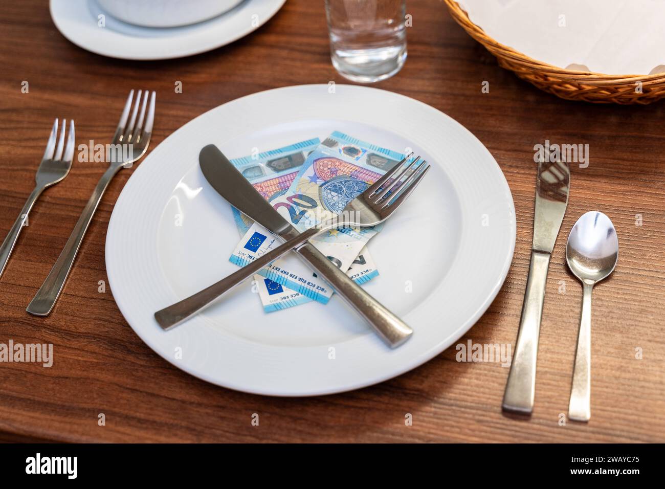 Bavière, Allemagne - 6 janvier 2024 : concept de coût de la nourriture et de gastronomie. Une table couchée avec une assiette blanche avec des billets en euros *** Kosten für Nahrung und Gastronomie Konzept. Ein gedeckter Tisch mit einem weißen Teller mit Euro Geldscheinen Banque D'Images