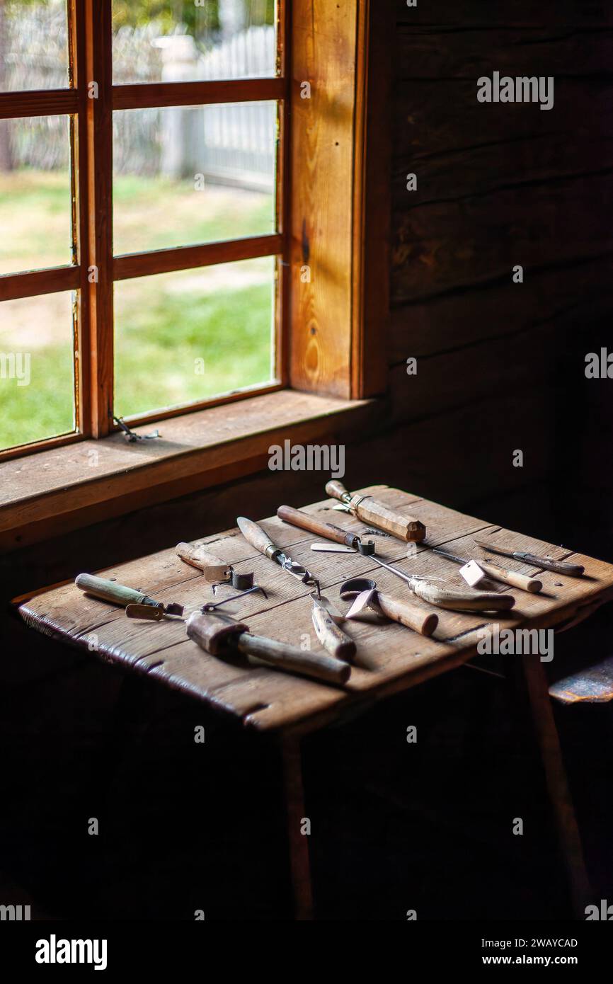 Un ensemble d'outils de sculpture sur bois anciens sur une table en bois près de la fenêtre. Le métier de fabriquer des sabots. Banque D'Images