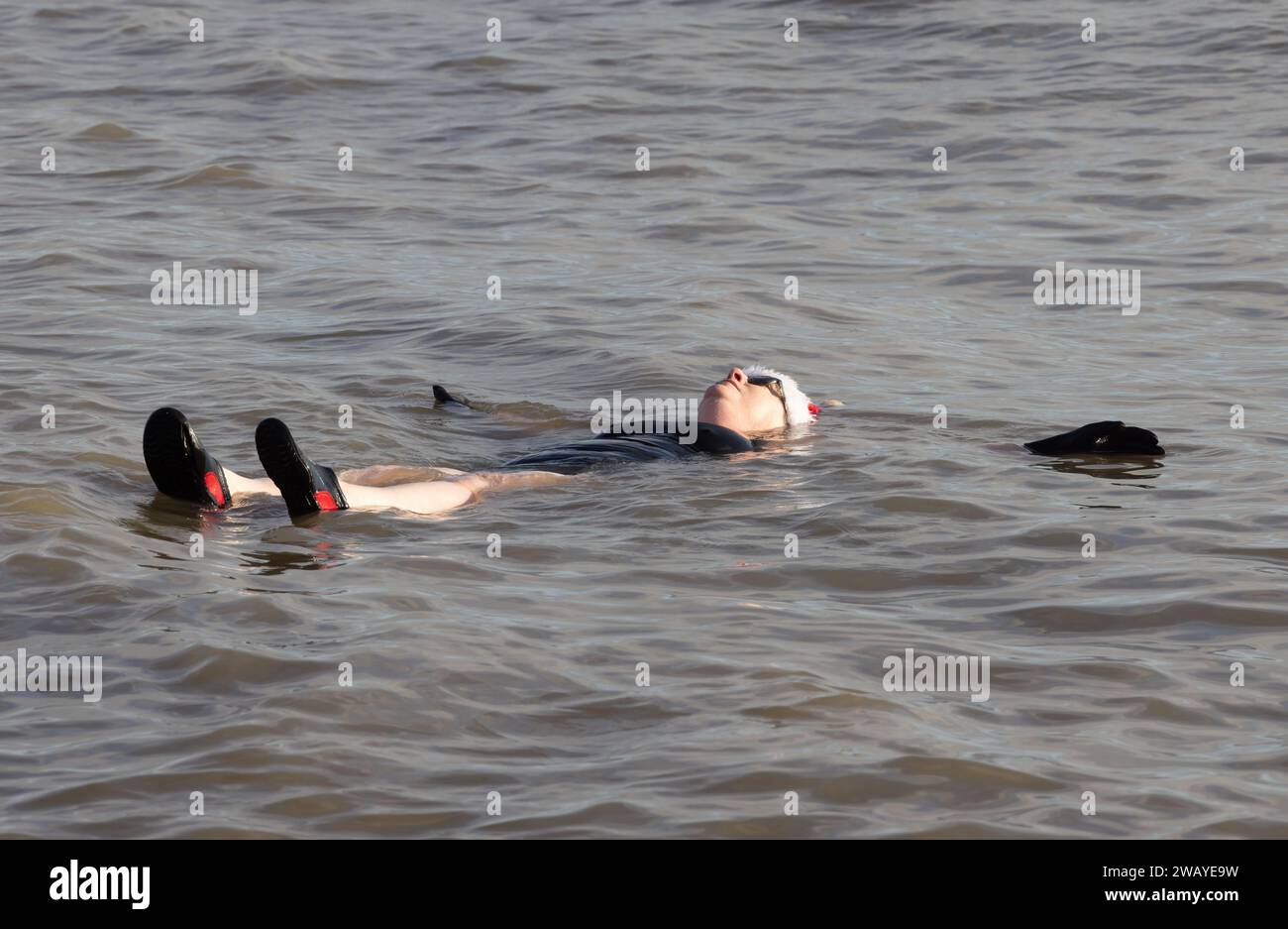 Femme flottant sur son dos dans la mer froide pendant la nage du lendemain de Noël d'Aldeburgh. Aldeburgh, Suffolk. ROYAUME-UNI Banque D'Images