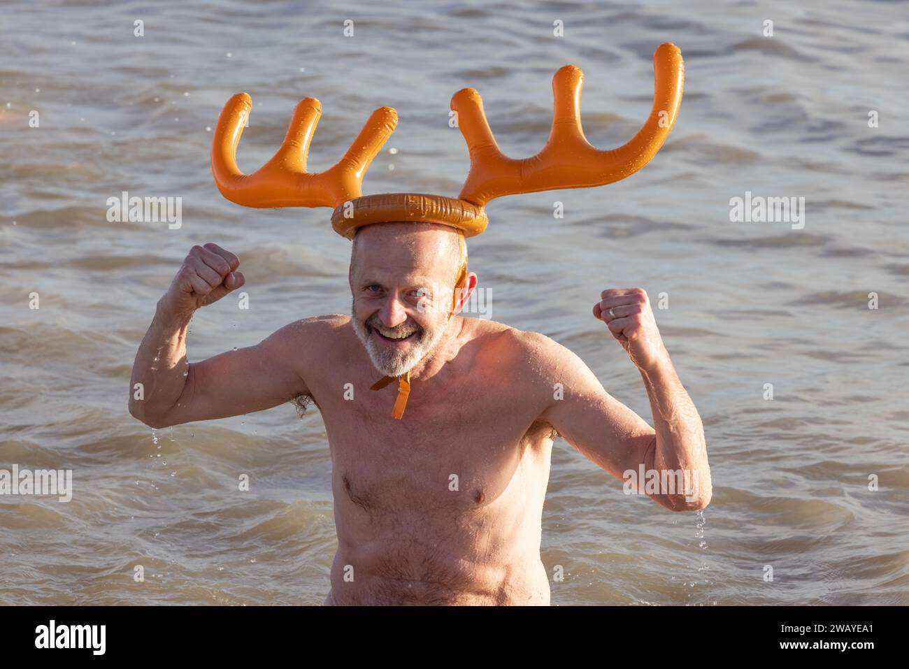 Homme heureux dans la mer avec chapeau de nouveauté participant à la natation de Boxing Day d'Aldeburgh. Aldeburgh, Suffolk. ROYAUME-UNI Banque D'Images