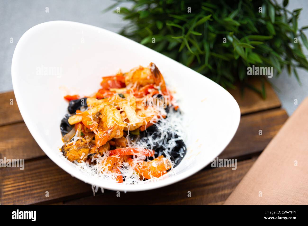 Pâtes penne à l'italienne mélangées à une riche sauce tomate, olives noires et saupoudrées de fromage râpé dans un bol blanc moderne. Banque D'Images
