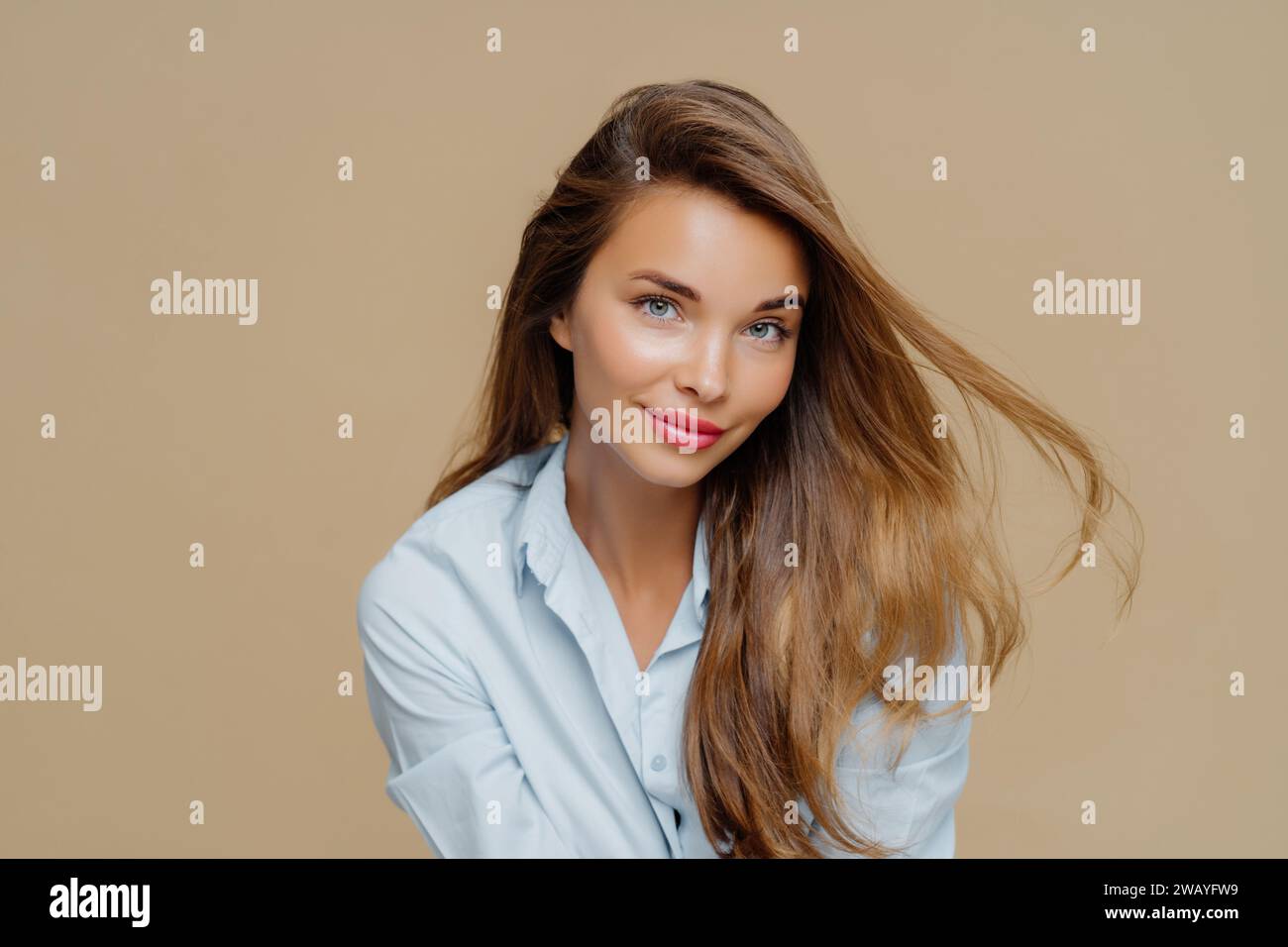 Brune balayée par le vent en chemise bleu clair, fond beige Banque D'Images