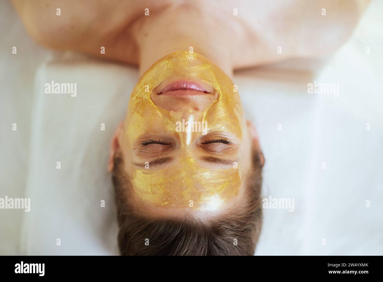 Le temps des soins de santé. Vue supérieure de la femme moderne détendue dans l'armoire de massage avec masque cosmétique doré sur le visage posé sur la table de massage. Banque D'Images