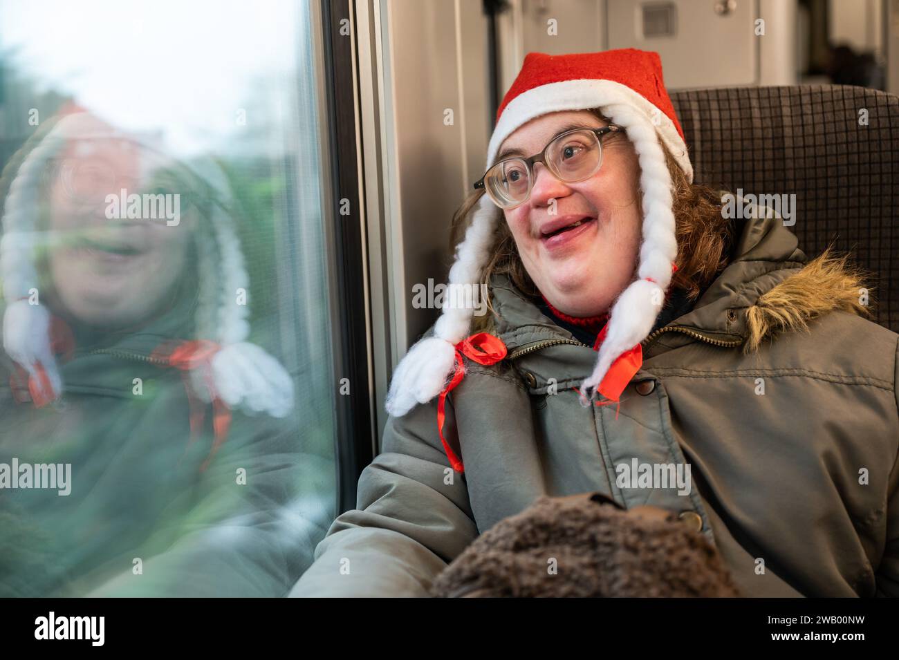 Heureuse femme de 41 ans avec le syndrome de Down, portant un chapeau de Noël, assise dans un train à Bruxelles, Belgique Banque D'Images