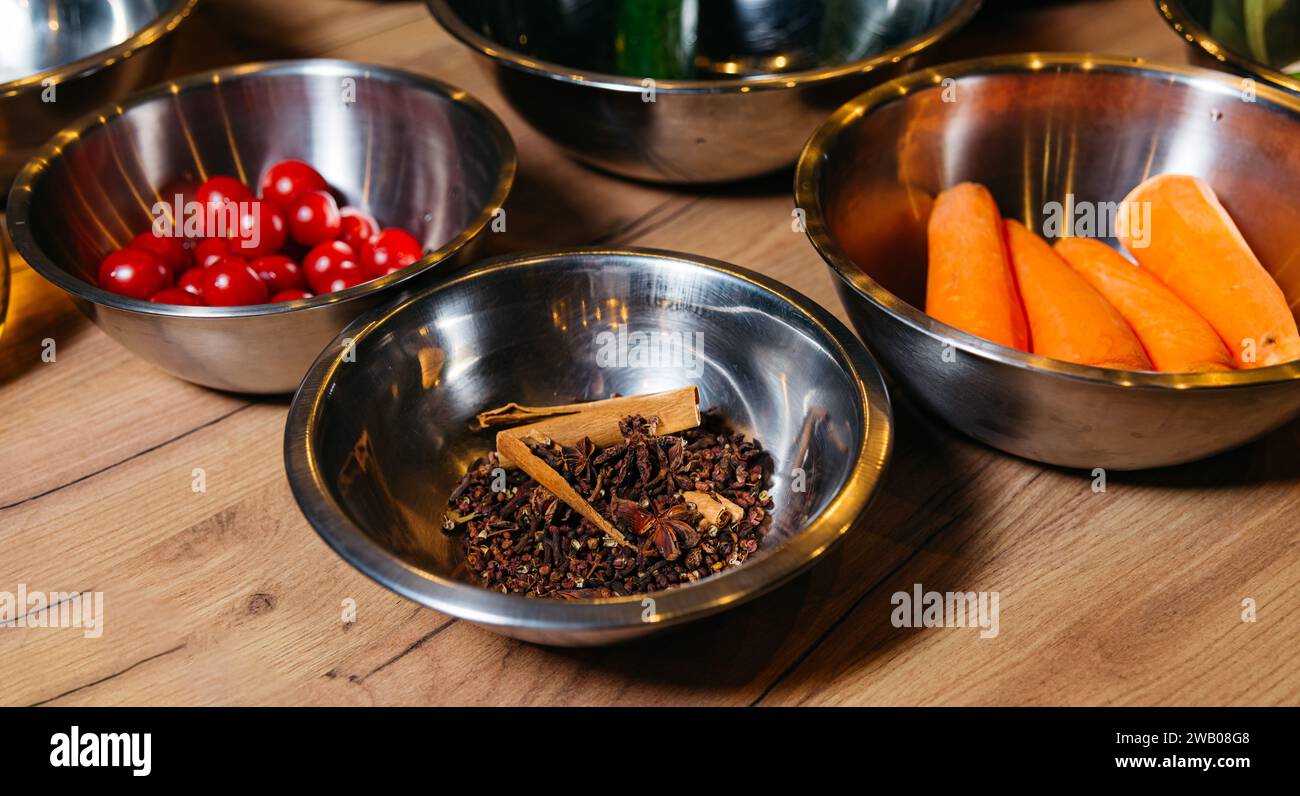 Bols en acier inoxydable remplis de tomates rouges éclatantes, de carottes pelées et d'épices entières aromatiques, prêts pour une séance de cuisine. Banque D'Images
