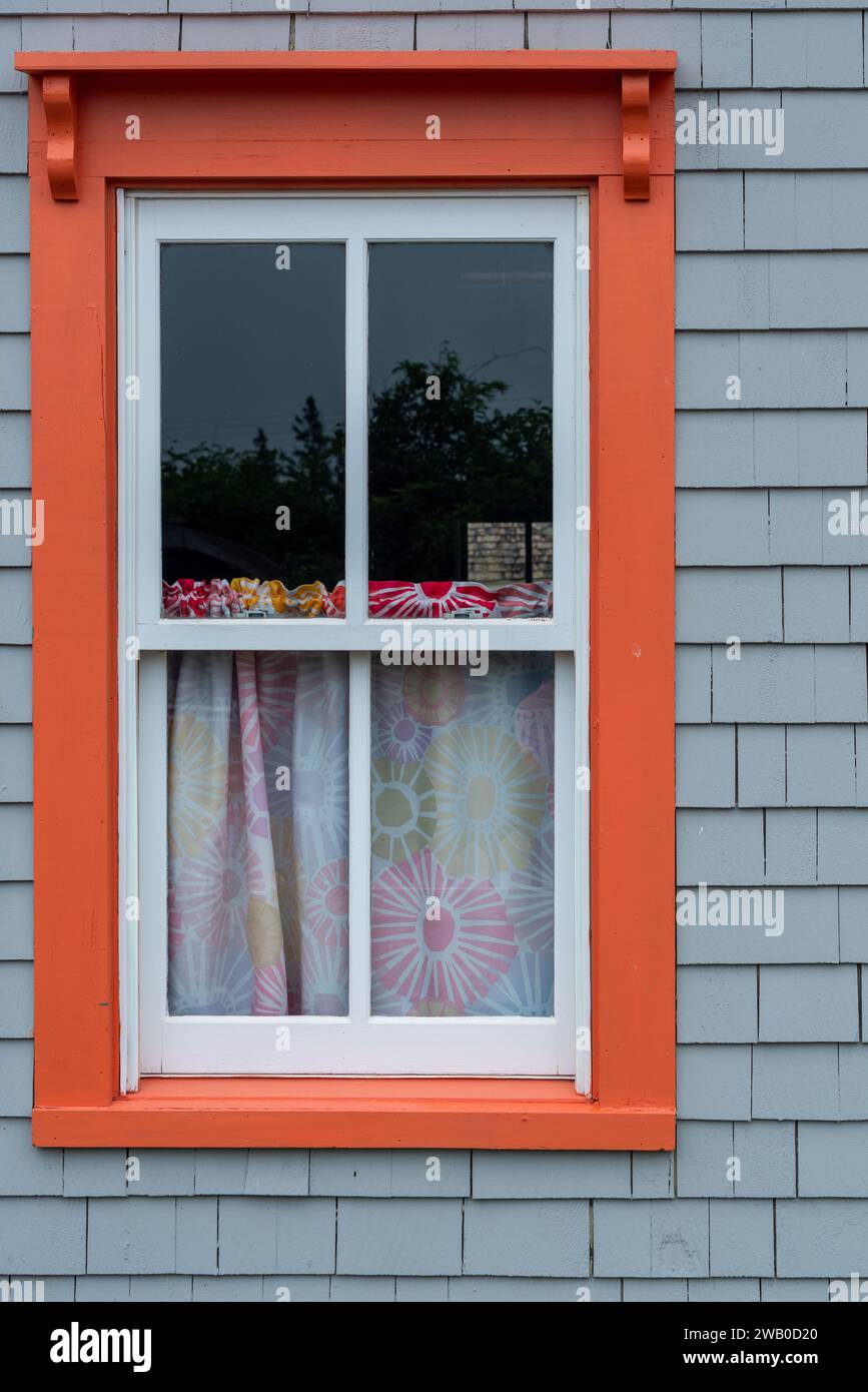 L'extérieur d'une maison en bois gris ou d'un mur de chalet est fait de shakes de cèdre. Il y a une seule fenêtre en verre vintage avec des garnitures décoratives en bois orange. Banque D'Images