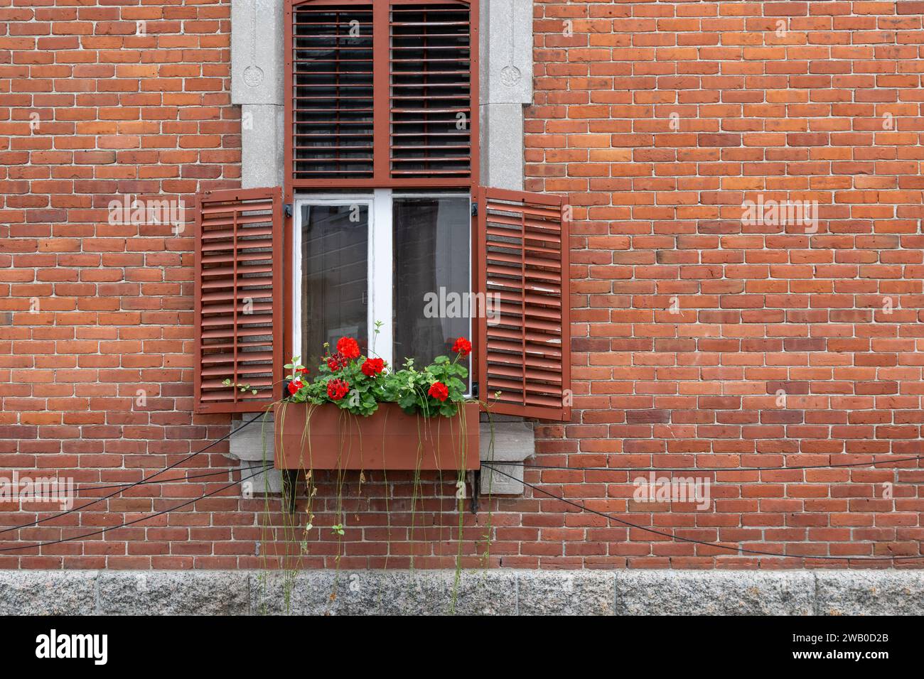 Le mur extérieur d'un immeuble d'appartements en briques rouges vintage avec une fenêtre décorée blanche. Il y a une boîte à fleurs en bois avec des fleurs de géranium rouge Banque D'Images