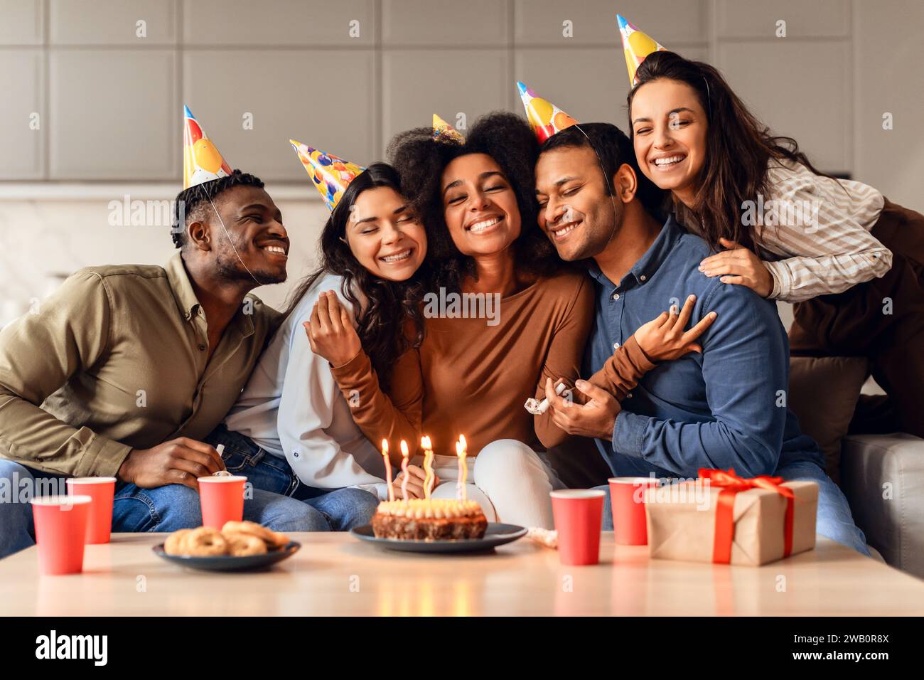 Joyeux amis multiculturels embrassant dame d'anniversaire célébrant et faisant la fête à l'intérieur Banque D'Images