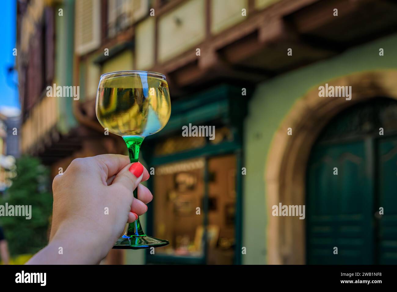 Main de femme avec un verre de vin Gewurztraminer dans un restaurant en plein air, maisons à colombages floues à Colmar France, route des vins d'Alsace village Banque D'Images Main de femme avec un verre de vin Gewurztraminer dans un restaurant en plein air, maisons à colombages floues à Colmar France, route des vins d'Alsace village Banque D'Images