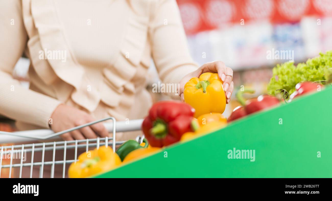 Femme poussant un chariot et achetant des légumes frais au supermarché, elle cueille un poivron Banque D'Images