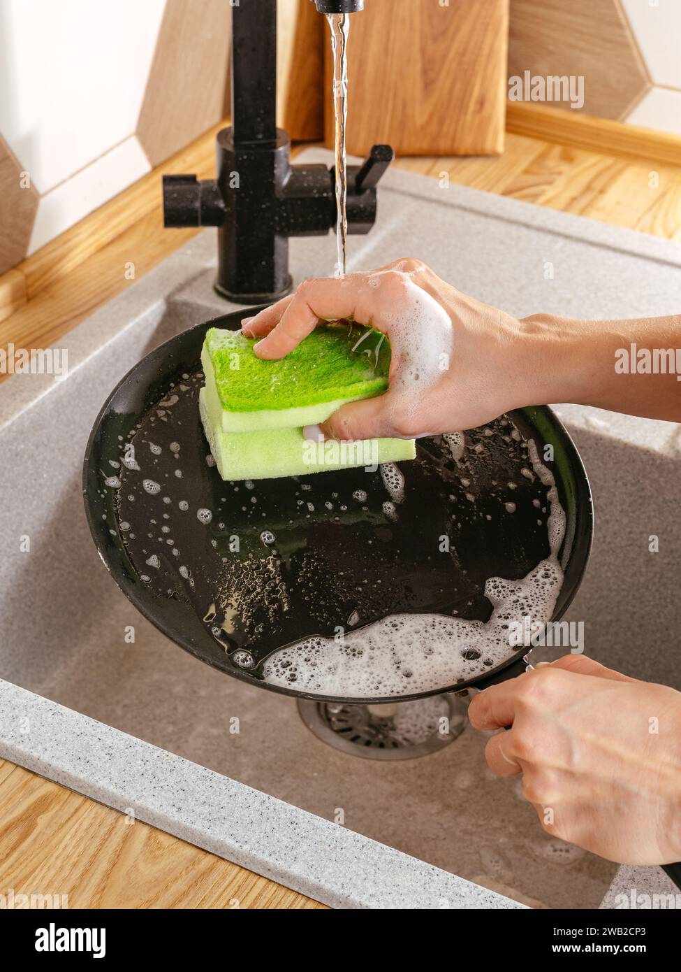 une fille lave une poêle avec une éponge à vaisselle Banque D'Images