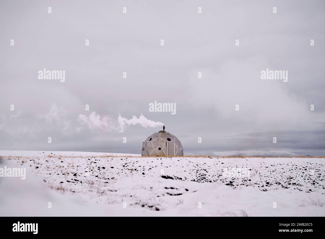 Igloo fumé sur terrain enneigé contre ciel nuageux en hiver Banque D'Images