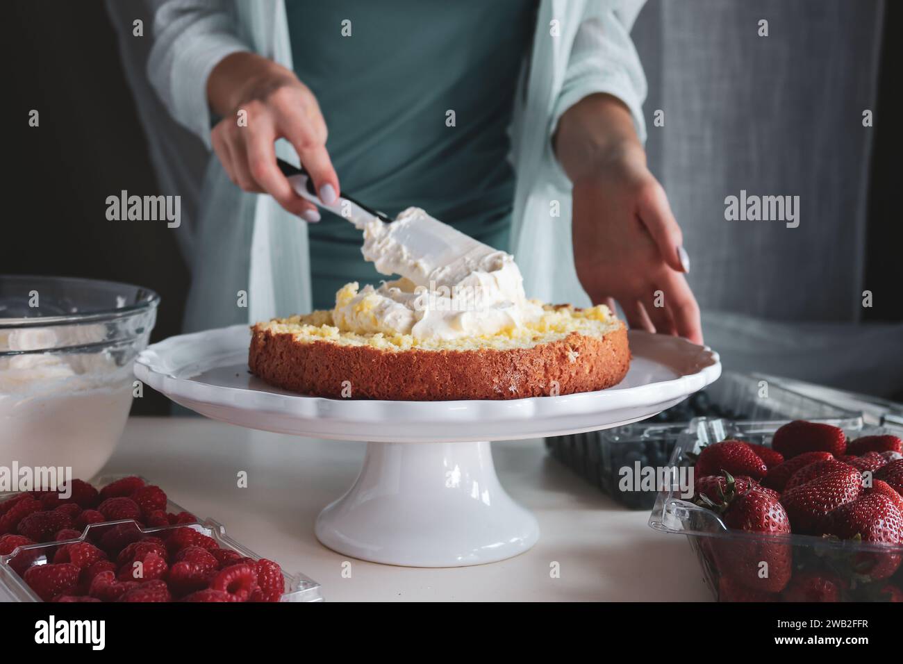 Baker étalant le glaçage sur une couche de gâteau de reddition par des fruits Banque D'Images