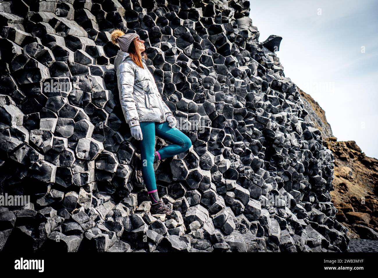 Une femme en manteau argenté et bonnet à côté des formations de basalte à Reynisfjara Banque D'Images