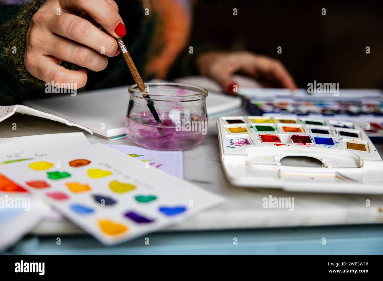 Détail des mains de la femme nettoyant la brosse à l'aquarelle dans l'eau avec des fournitures d'art. Banque D'Images