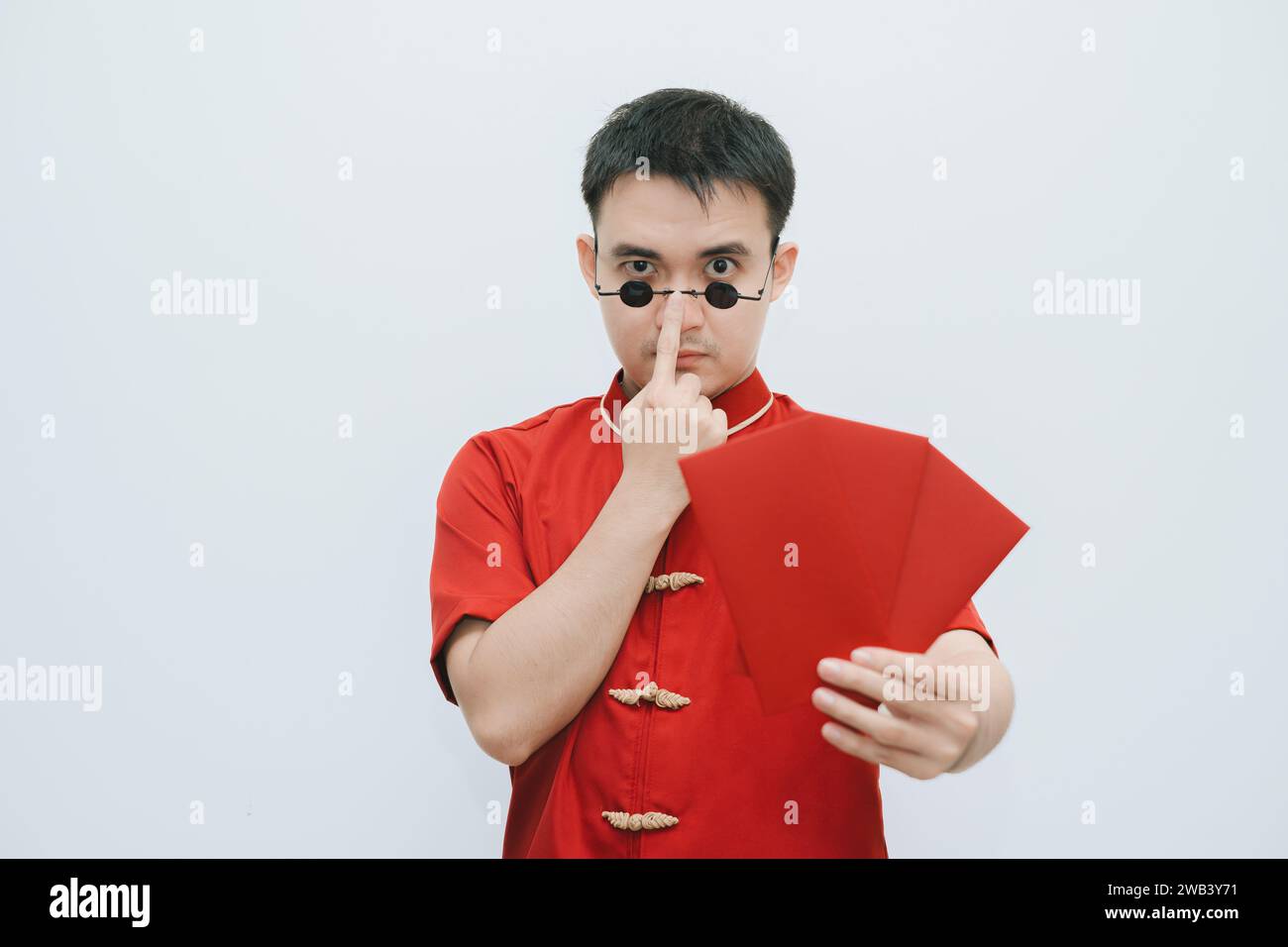 Homme asiatique portant Cheongsam et lunettes de soleil vintage noir tient et montre angpao ou cadeau monétaire rouge à l'appareil photo sur fond blanc Banque D'Images