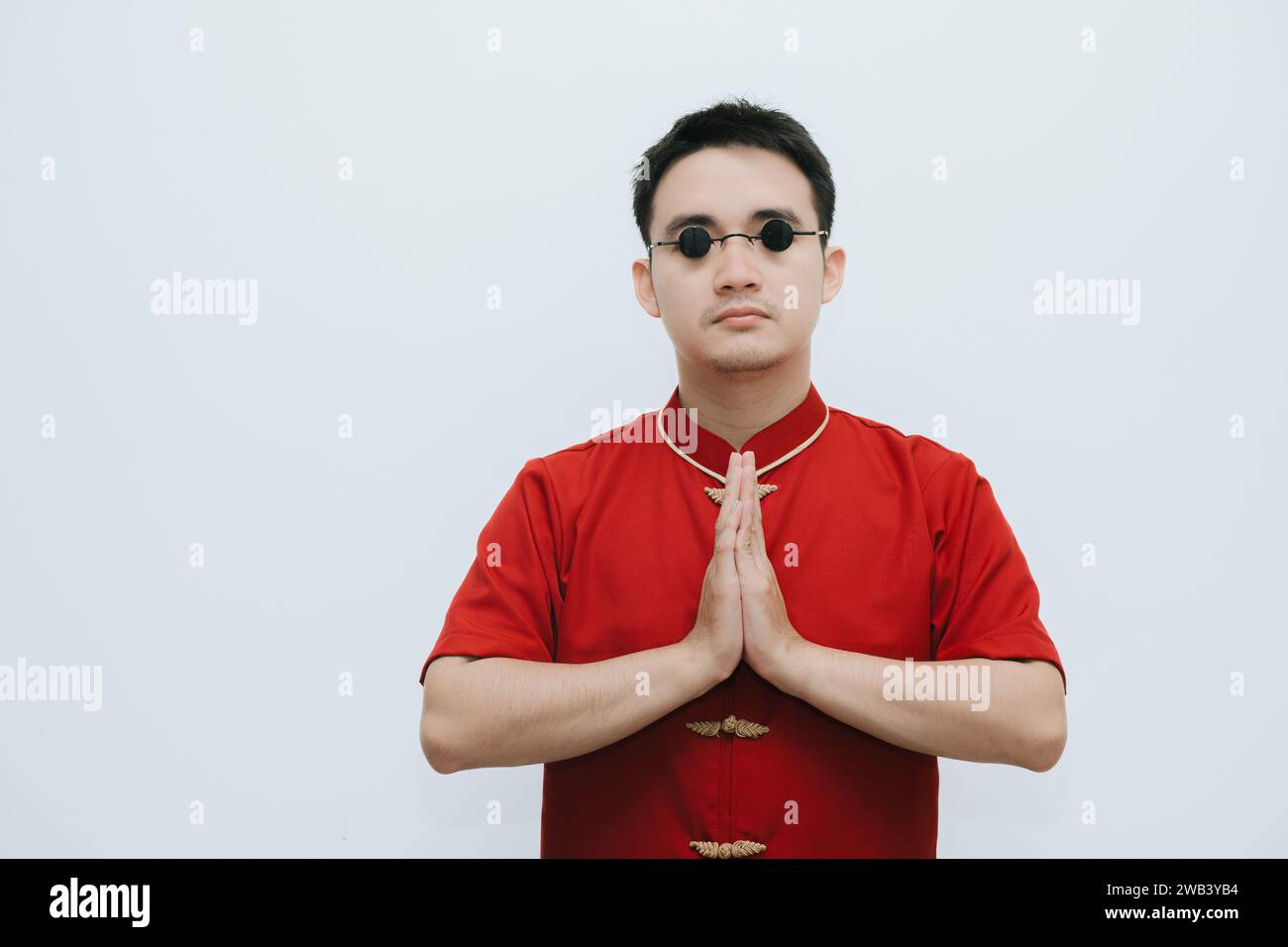 Homme asiatique portant Cheongsam et lunettes de soleil vintage noir est sur le namaste ou geste de bienvenue ou de salutation à la caméra sur fond blanc Banque D'Images