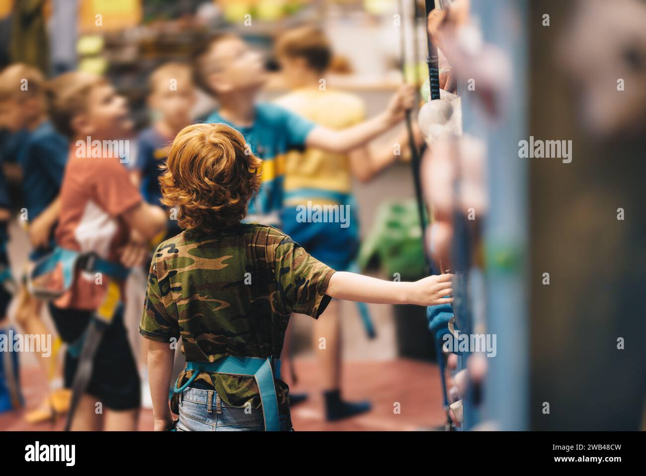 Groupe d'enfants d'école à un cours d'escalade en salle. Petit garçon grimpant un mur de roche à l'intérieur. Cours de formation de bloc pour les enfants d'école Banque D'Images