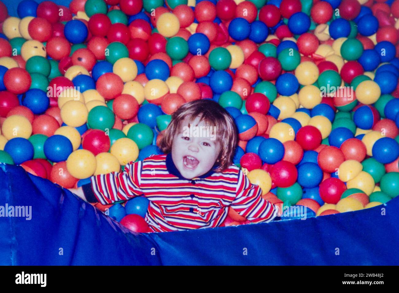 Photo d'archives de 1994. Jeune fille enfant en bas âge jouant dans la fosse à balle, s'amuser à jouer avec des balles colorées. Banque D'Images