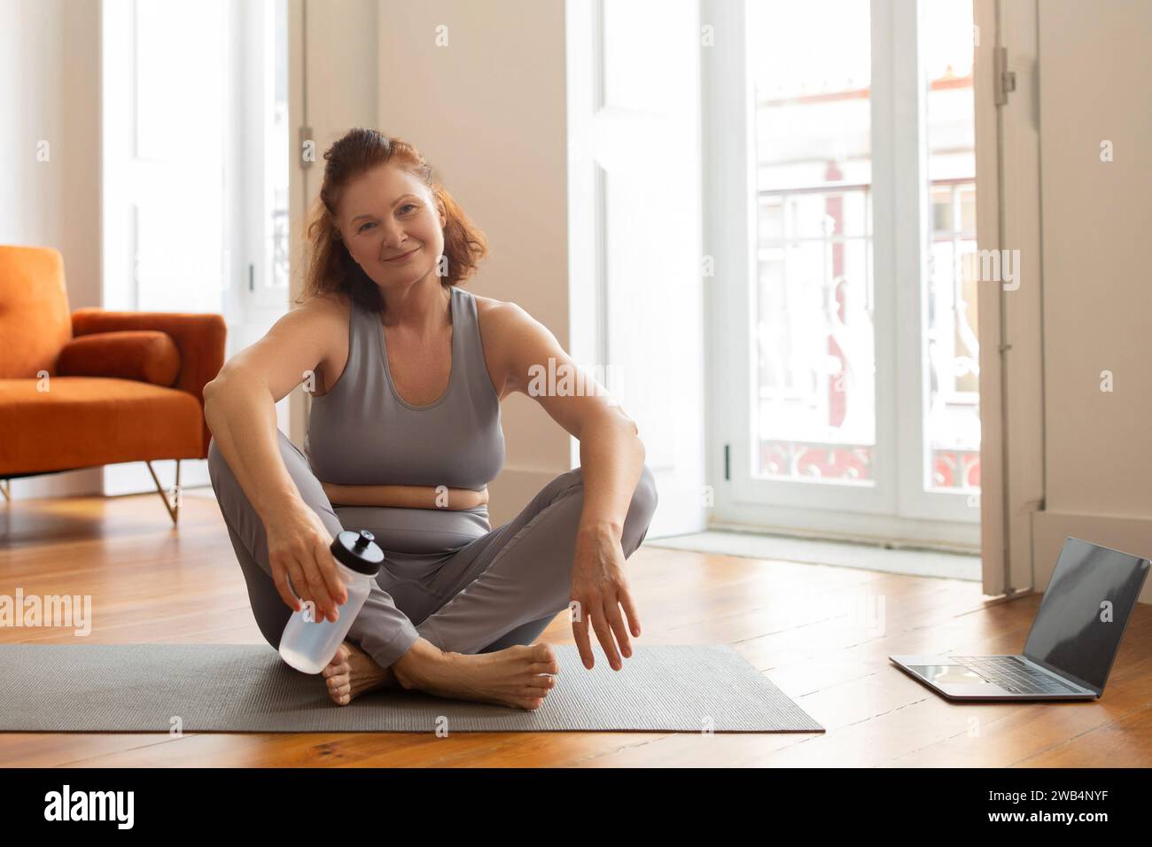Femme âgée se reposant avec de l'eau après l'entraînement de fitness à la maison Banque D'Images