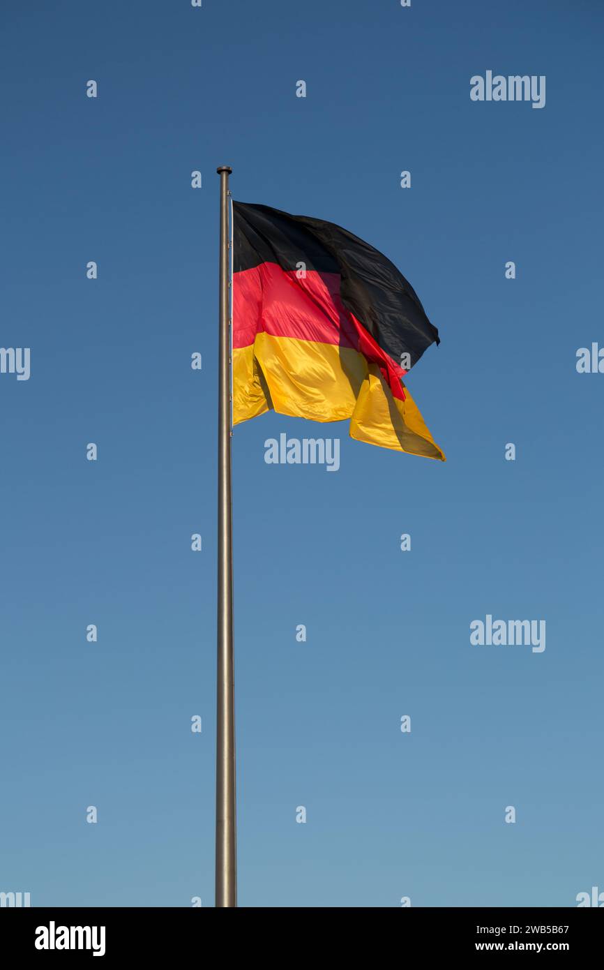 Drapeau allemand sur un mât contre le ciel bleu, drapeau national de l'Allemagne. Banque D'Images