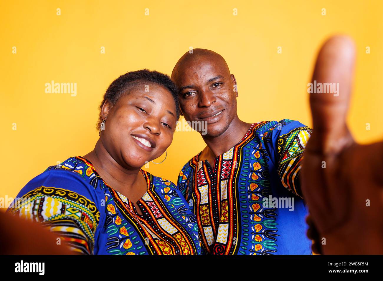 Homme noir souriant et femme portant des vêtements ethniques prenant selfie sur smartphone et regardant la caméra avant. Joyeux couple tenant le téléphone portable et faisant le portrait pov photo Banque D'Images