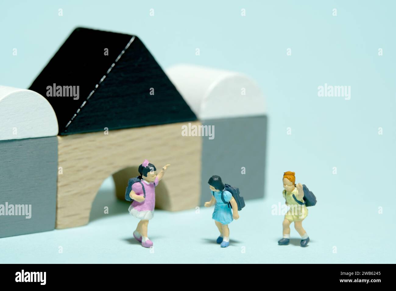Photographie miniature de figurine de jouet de personnes. Filles élèves de maternelle jouant au bloc de bois Montessori. Isolé sur fond bleu. Image photo Banque D'Images