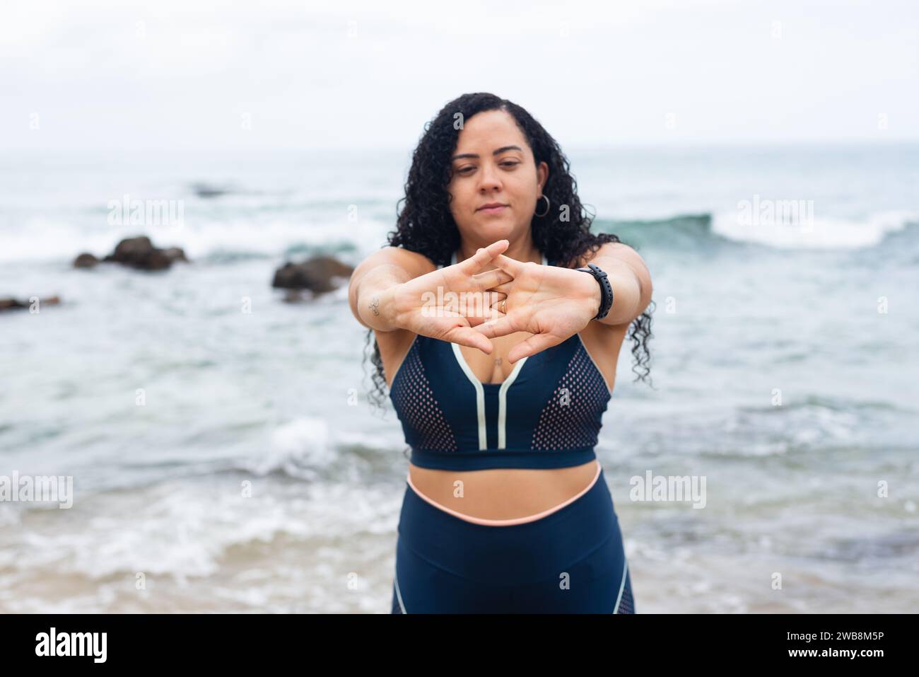Jeune femme de fitness faisant des exercices avec ses mains sur le sable de plage contre la mer et le ciel nuageux. Mode de vie sain. Banque D'Images