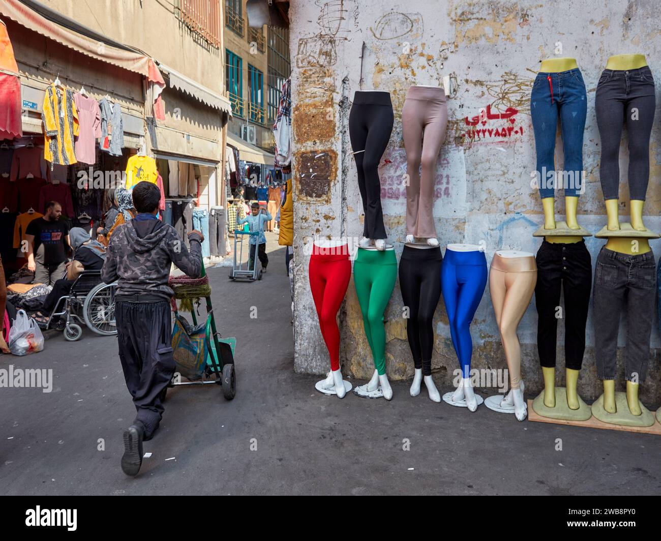 Un portier passe devant une exposition de pantalons et de leggings pour femmes sur les jambes de mannequins féminins dans la région du Grand Bazar à Téhéran, en Iran. Banque D'Images