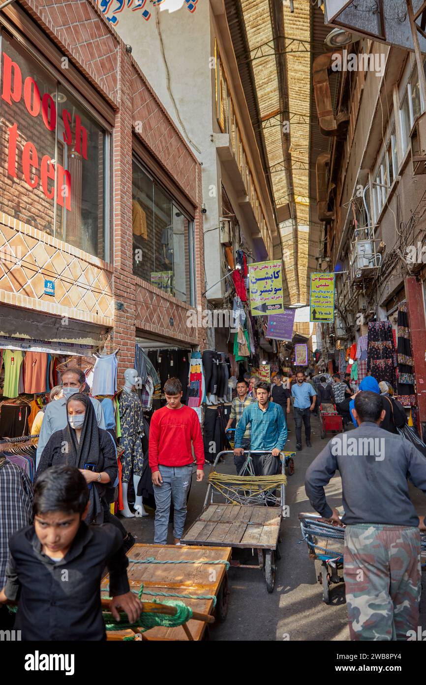 Les porteurs poussent leurs charrettes le long d’une rue étroite couverte dans la zone du Grand Bazar à Téhéran, en Iran. Banque D'Images