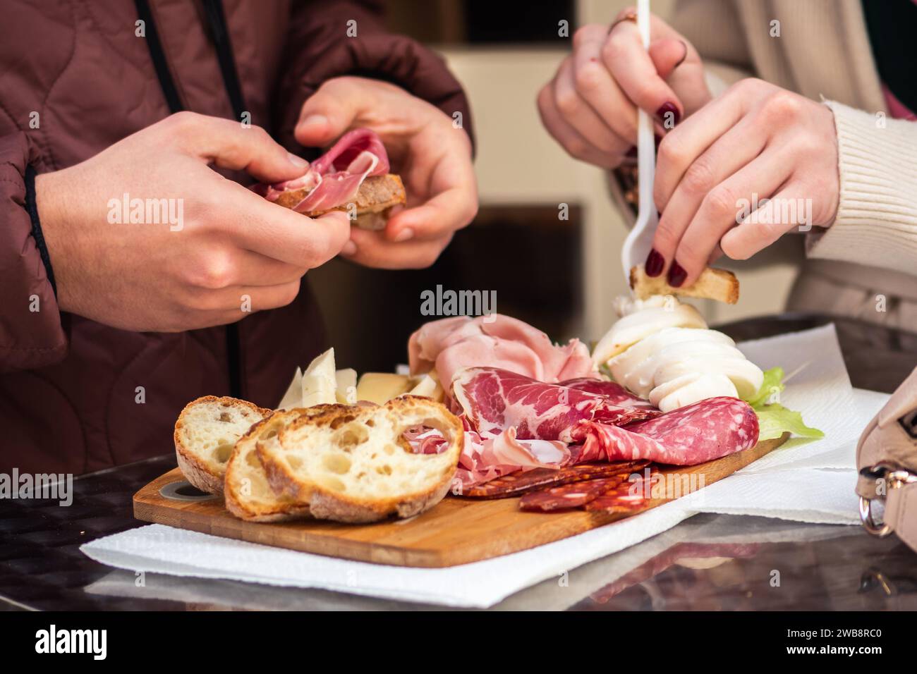 Couple de touristes mangeant un mélange de charcuterie, fromage, mozzarella avec des tranches de pain placées sur une planche de bois Banque D'Images