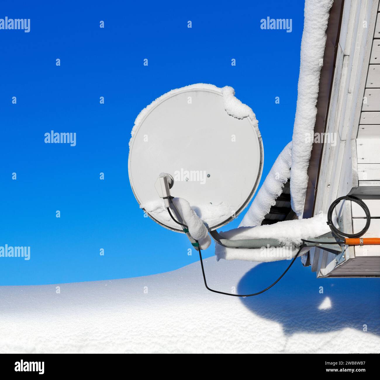 Antenne parabolique couverte de neige, contre du ciel bleu. Banque D'Images