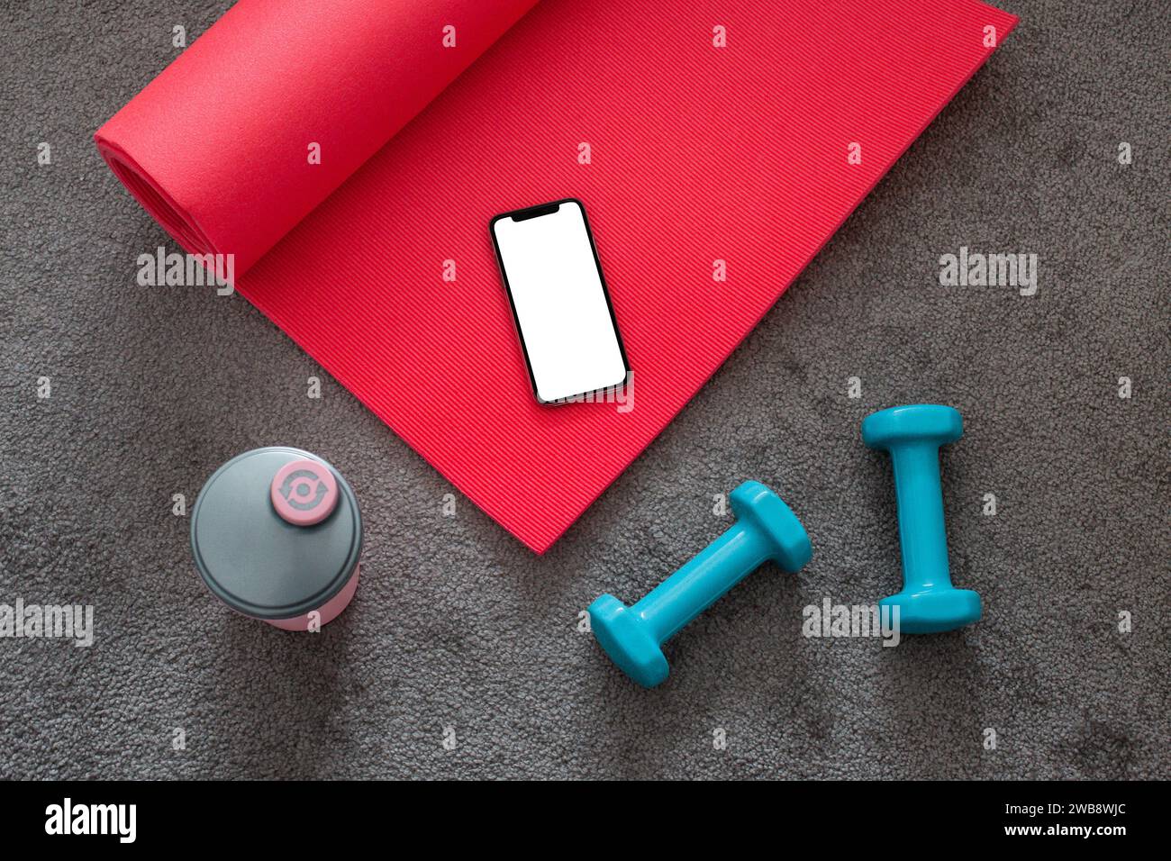 Vue de dessus du tapis de yoga rose, haltères bleus équipement de fitness sur tapis gris avec téléphone portable. Banque D'Images