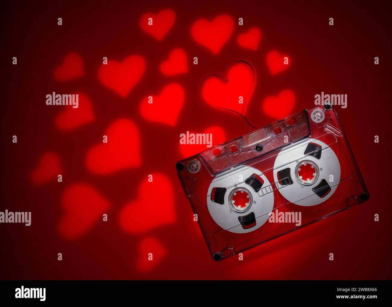 Cassette audio transparente avec ruban en forme de coeur à l'extérieur et avec beaucoup de projections de coeur de lumière rouge en arrière-plan. Banque D'Images