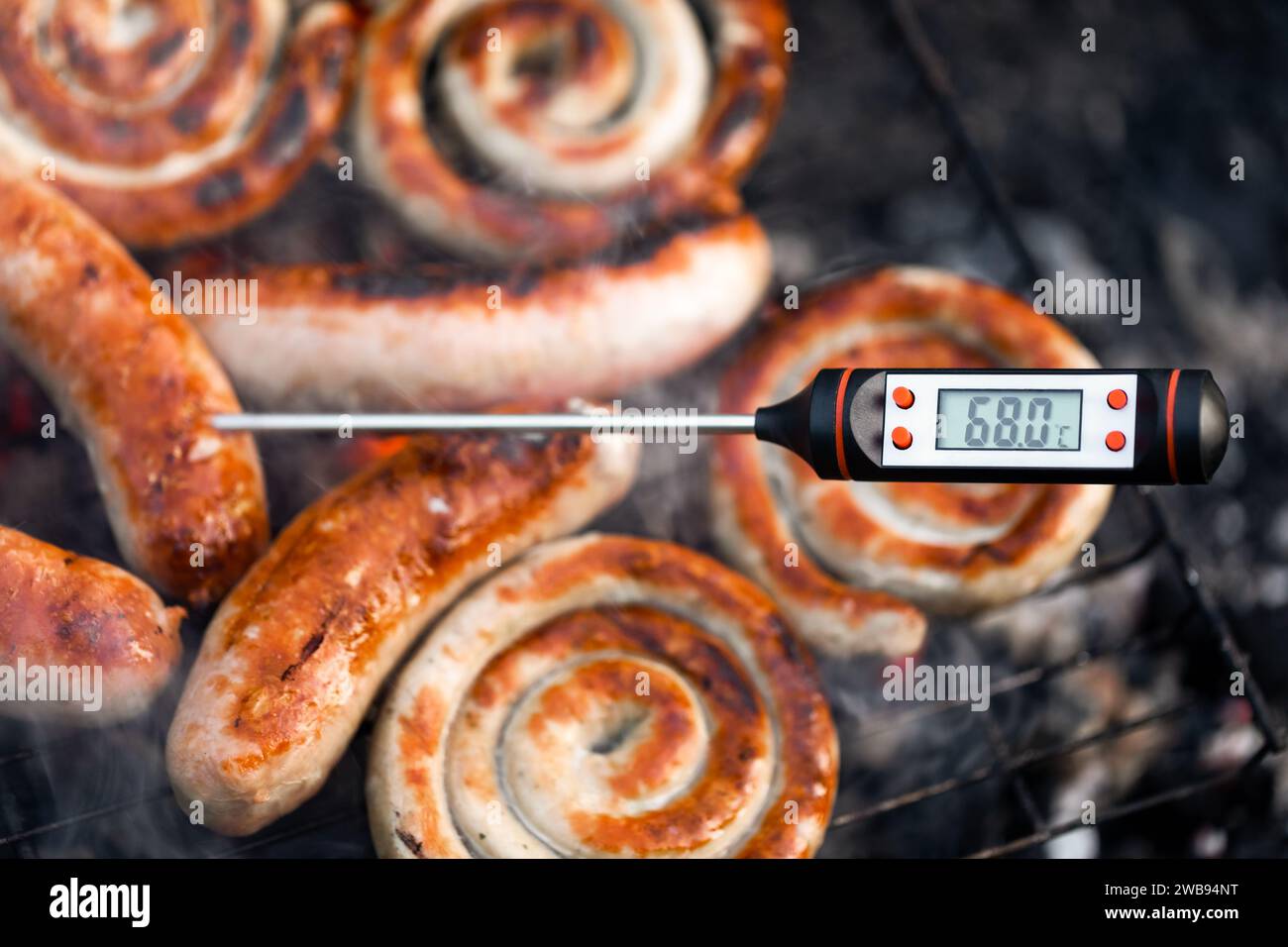 Сlose-plan d'un thermomètre à viande numérique affichant une température de cuisson sécuritaire des saucisses cuites sur un gril à fumée Banque D'Images