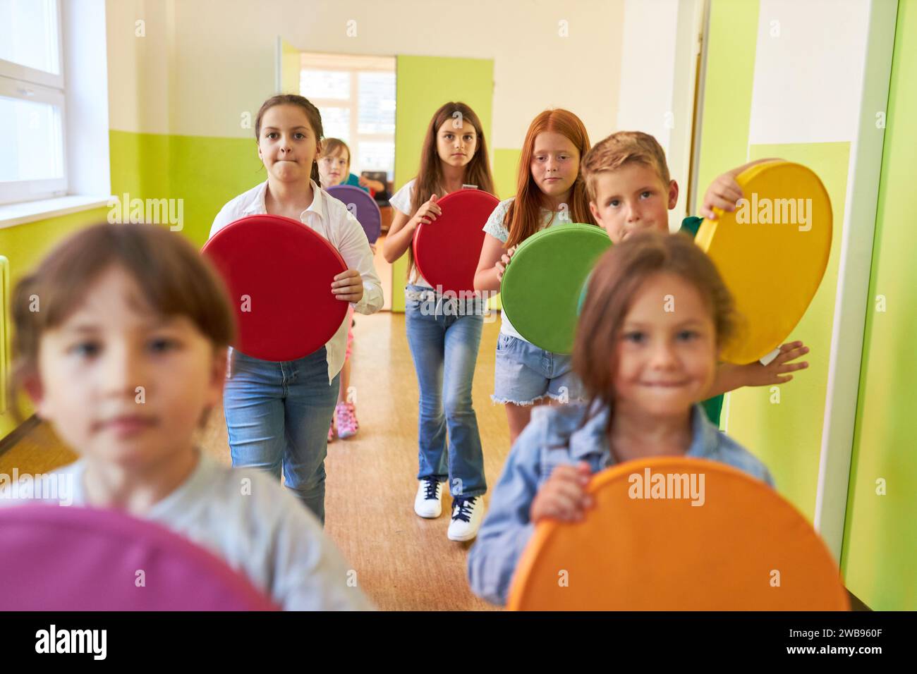 Groupe d'enfants tenant des coussins colorés tout en marchant dans le couloir à l'école Banque D'Images