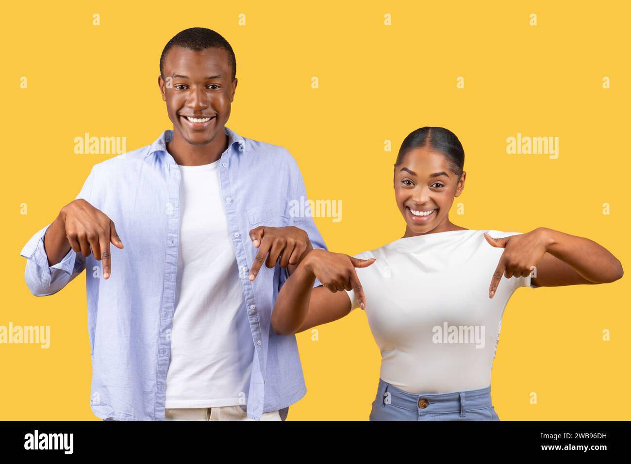 Joyeux couple noir pointant vers le bas, sourires fiers, fond jaune Banque D'Images