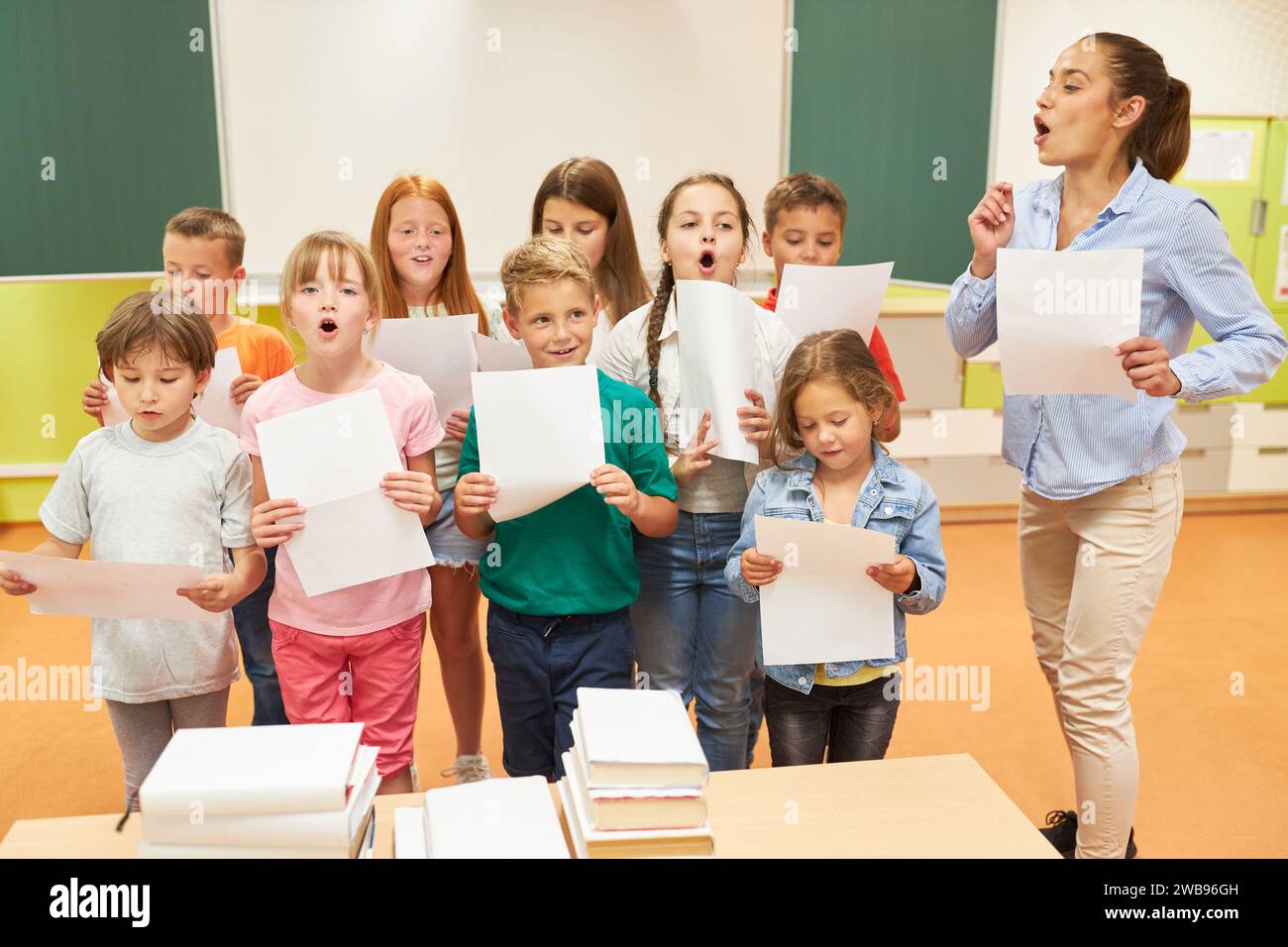 Enfants de l'école primaire chantant chœur avec enseignante debout dans la salle de classe Banque D'Images Enfants de l'école primaire chantant chœur avec enseignante debout dans la salle de classe Banque D'Images