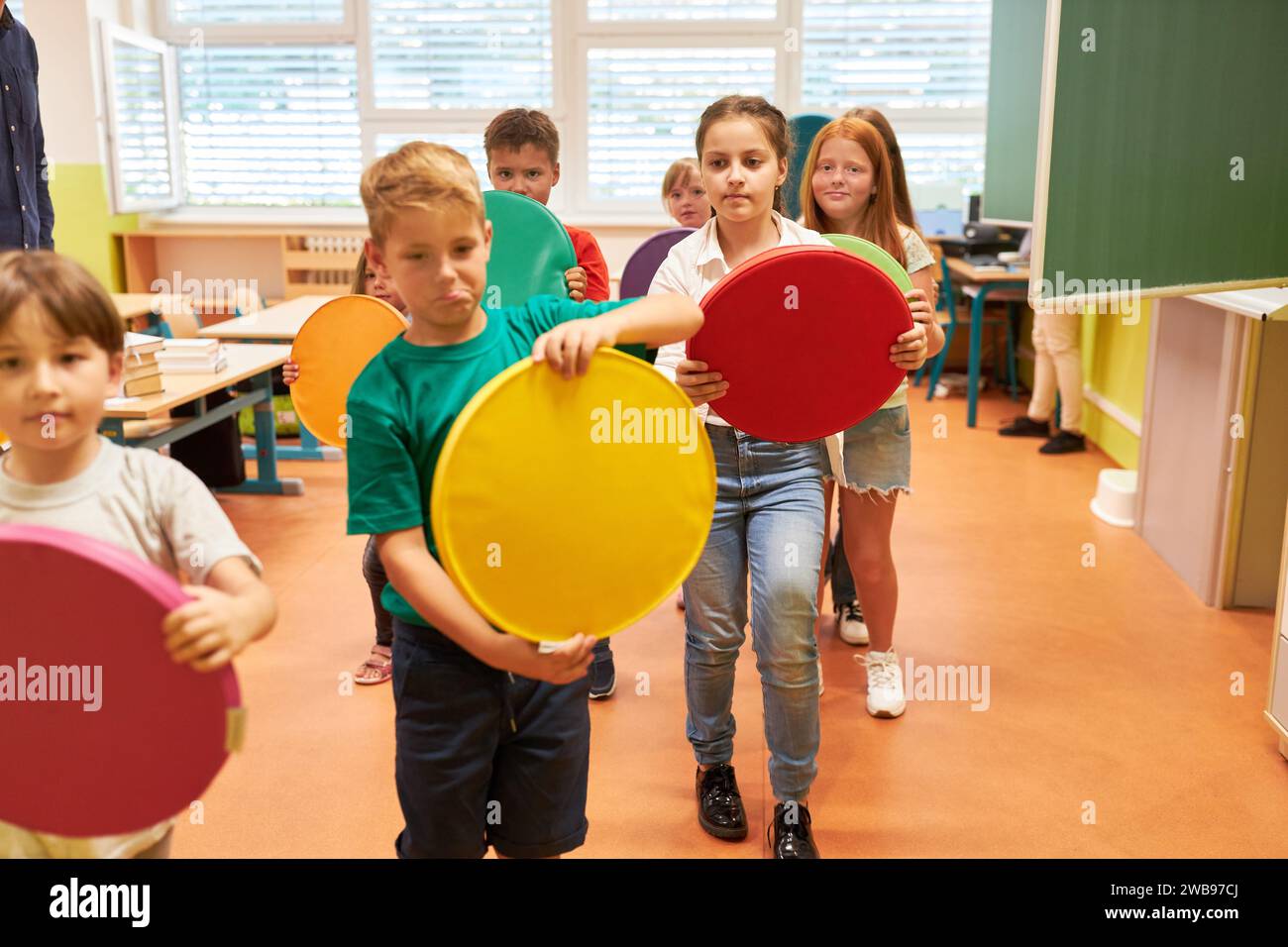 Groupe d'écoliers élémentaires marchant tout en tenant des coussins de siège colorés dans la salle de classe Banque D'Images