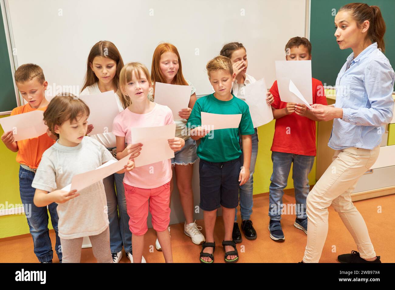 Professeur d'école primaire chantant chœur avec les élèves tenant la feuille tout en se tenant debout dans la salle de classe Banque D'Images Professeur d'école primaire chantant chœur avec les élèves tenant la feuille tout en se tenant debout dans la salle de classe Banque D'Images