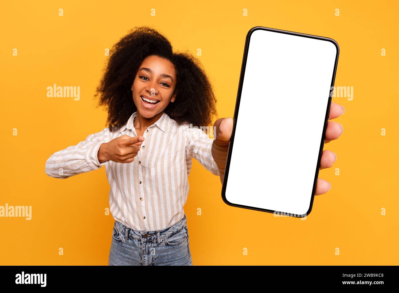 Femme noire heureuse présentant l'écran de smartphone sur fond jaune Banque D'Images